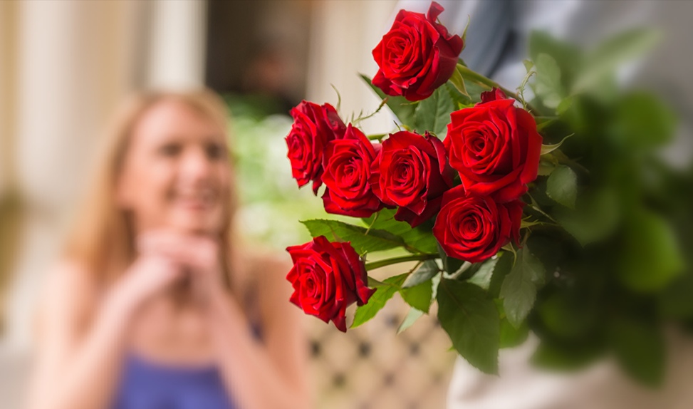 Young woman looking at man with flower bouquet behind the back.