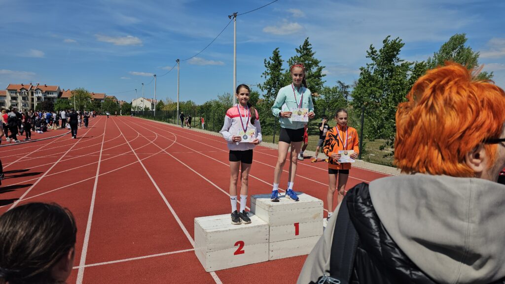 Dvoje mladih atletičara na pobedničkom postolju tokom takmičenja na atletskom stadionu.
