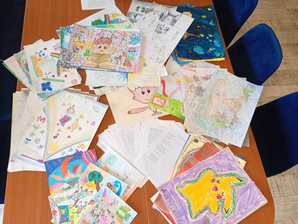 Raznobojne dečje crteže i radove razbacane po stolu.