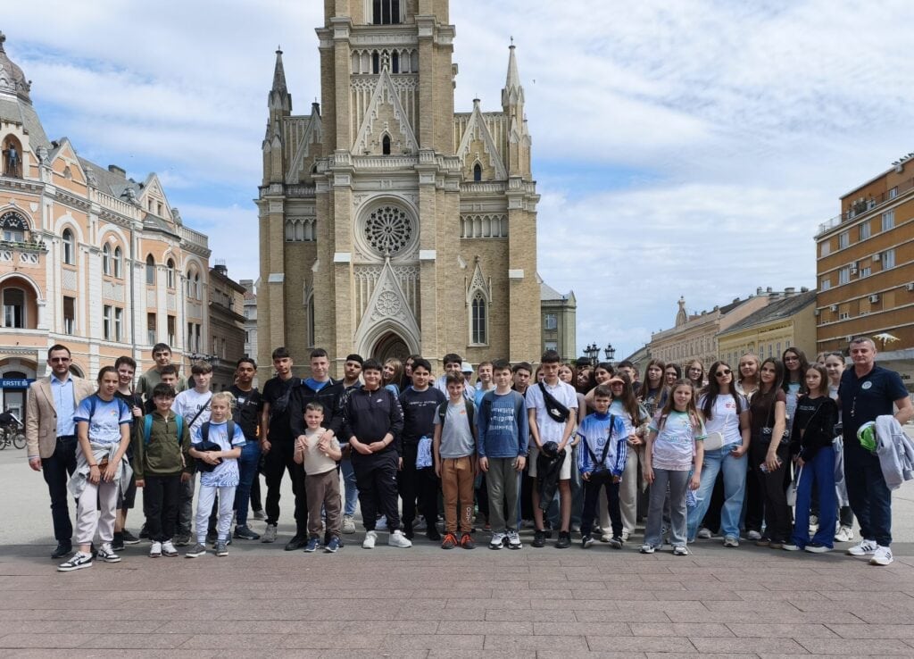 Vesela grupa učenika ispred crkve u Požarevcu, spremni za školsku ekskurziju ili izlet.