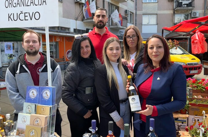Prijateljska grupa ljudi na sajmu u Požarevcu, uz promociju lokalnih vina i proizvoda, ispred zgrade.