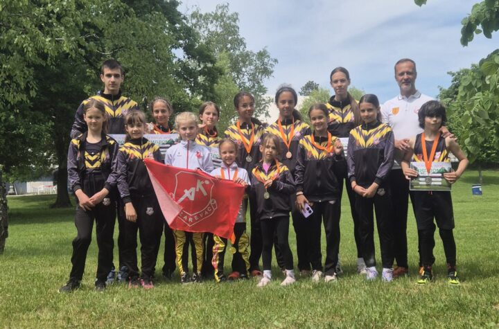 Omladinci sa medaljama i zastavom na terenu u prirodi.